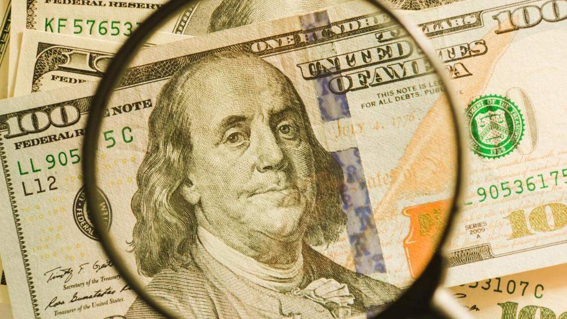 Inspecting of hundred-dollar bills through a magnifying glass.