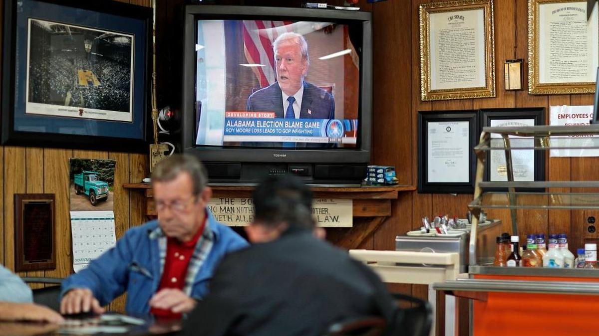 A newscast showing President Donald Trump played on an old television set as customers play cards in the Frosty Freeze restaurant in Sandy Hook Dec. 14, 2017. Many families here can trace their ancestry back generations on the same land. Almost everyone is white, and almost everyone is Christian. At the Frosty Freeze, a plaque with a Bible verse hangs under the television, from the book of Romans: "Owe no man nothing but to love one another."