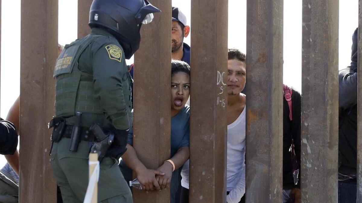 Migrants from Central America yell through a border wall at a U.S. Border Patrol agent after he pulled down a banner Sunday, Nov. 25, 2018, in San Diego. Migrants approaching the U.S. border from Mexico were enveloped with tear gas after a few tried to breach the fence separating the two countries. (AP Photo/Gregory Bull)