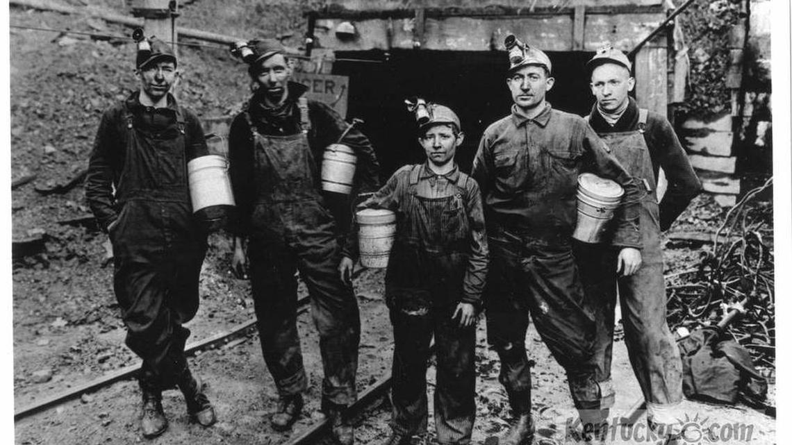 In this undated historic photo, coal miners pause at mine entry in Lynch in Harlan County. Round lunch pails are triple-tiered to hold both food and water. Carbide lamps are mounted atop soft headgear which actually only served to hold the lights and offered no protection.