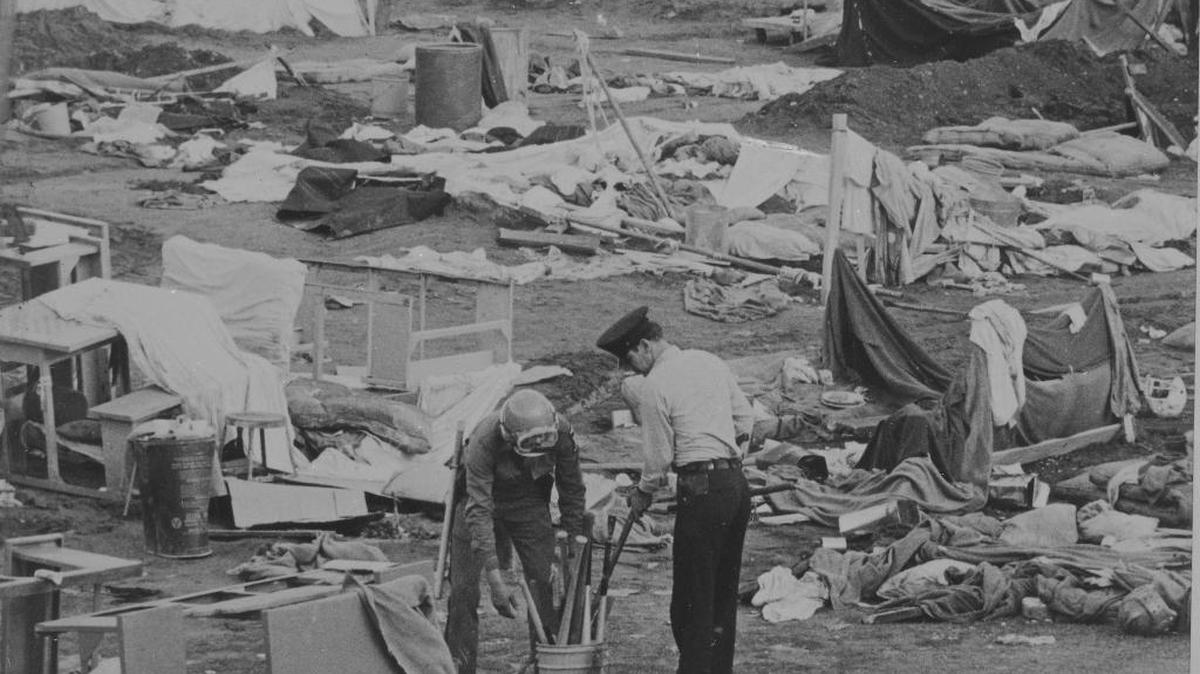 A policeman and guard collect baseball bats and other possible weapons from the exercise yard in the Attica State Prison, Attica, N.Y., Sept. 14, 1971, in exercise yard "D" where rioting prisoners had set up a stronghold and held 38 hostages for five days. In the background are makeshift shelters made by the inmates to protect themselves from the rain.