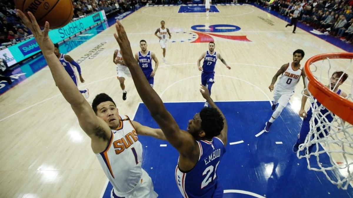 Phoenix Suns' Devin Booker (1) goes up for a shot against Philadelphia 76ers' Joel Embiid (21) during the first half of an NBA basketball game, Monday, Dec. 4, 2017, in Philadelphia. Phoenix won 115-101.