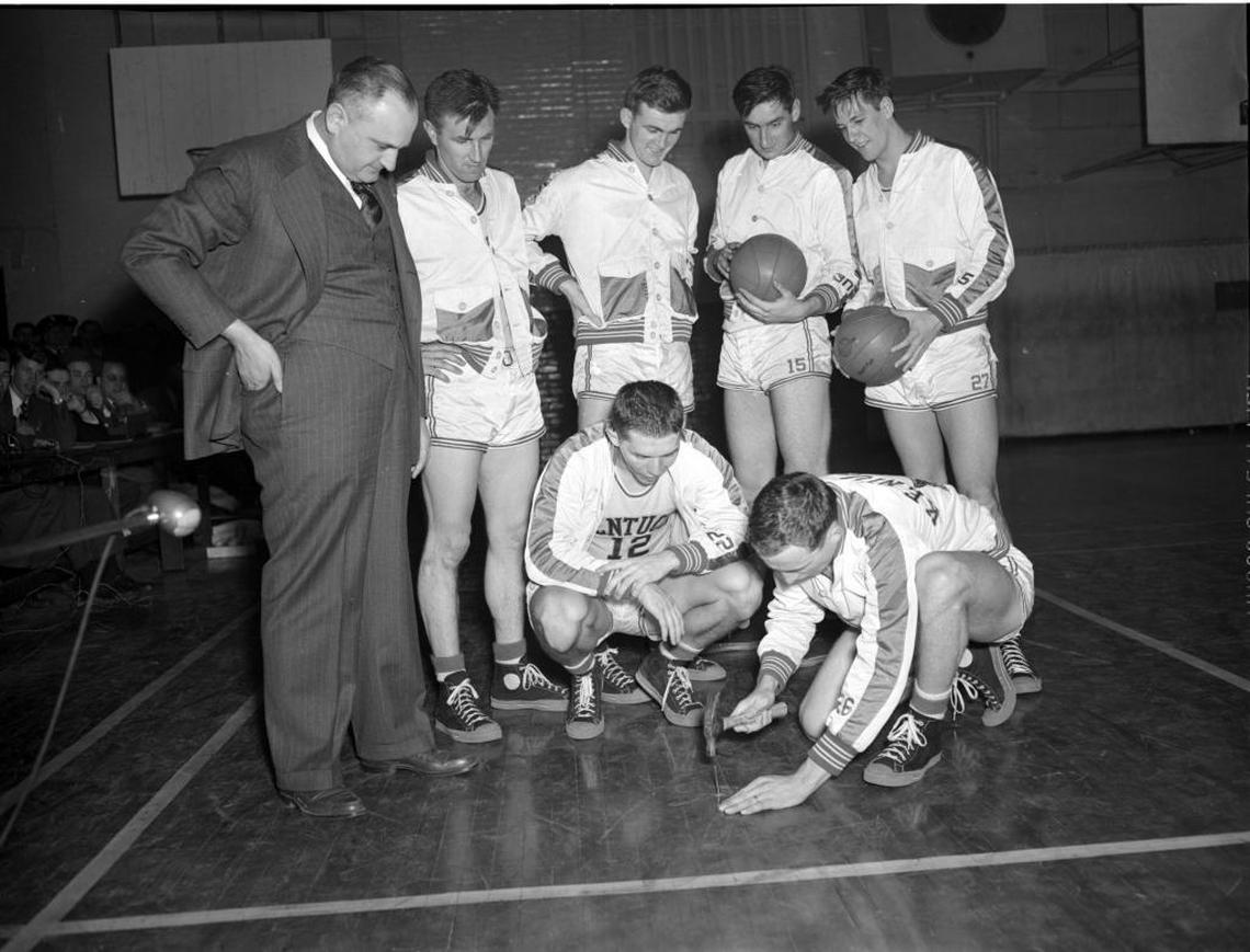 The UK team gathered at Alumni Gym in 1948 to mark a spectacular shot by the Wildcats’ Ralph Beard with a nail in the floor. The nail marked the spot from which Beard launched a 54-foot shot in a 69-42 win against Tennessee on Feb. 14, 1948. Beard (12) was crouching at the center of the photo. Standing, from left, were Coach Adolph Rupp, Cliff Barker, Joe Holland, Alex Groza and Wah Wah Jones. Driving in the nail was team captain Kenny Rollins.