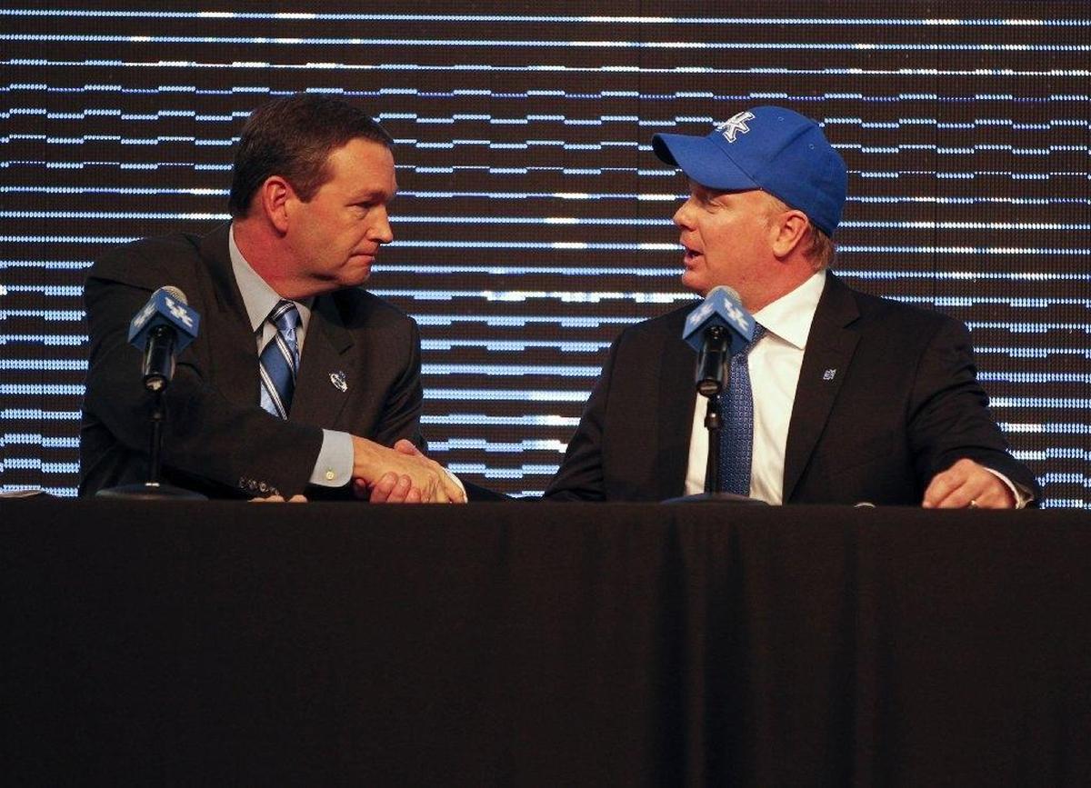 Kentucky Athletics Director Mitch Barnhart, left, shakes hands with Mark Stoops on Dec. 2, 2012, at the news conference where Stoops was introduced as UK’s football coach.