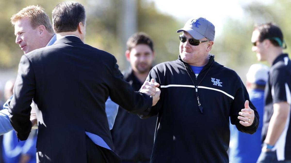 UK basketball coach John Calipari, left, shook hands with head UK football coach Mark Stoops as the UK football team practiced at the E.J. Nutter Training Facility April 23, 2014. On the left is one of Mark Stoops’ brothers, Mike Stoops.