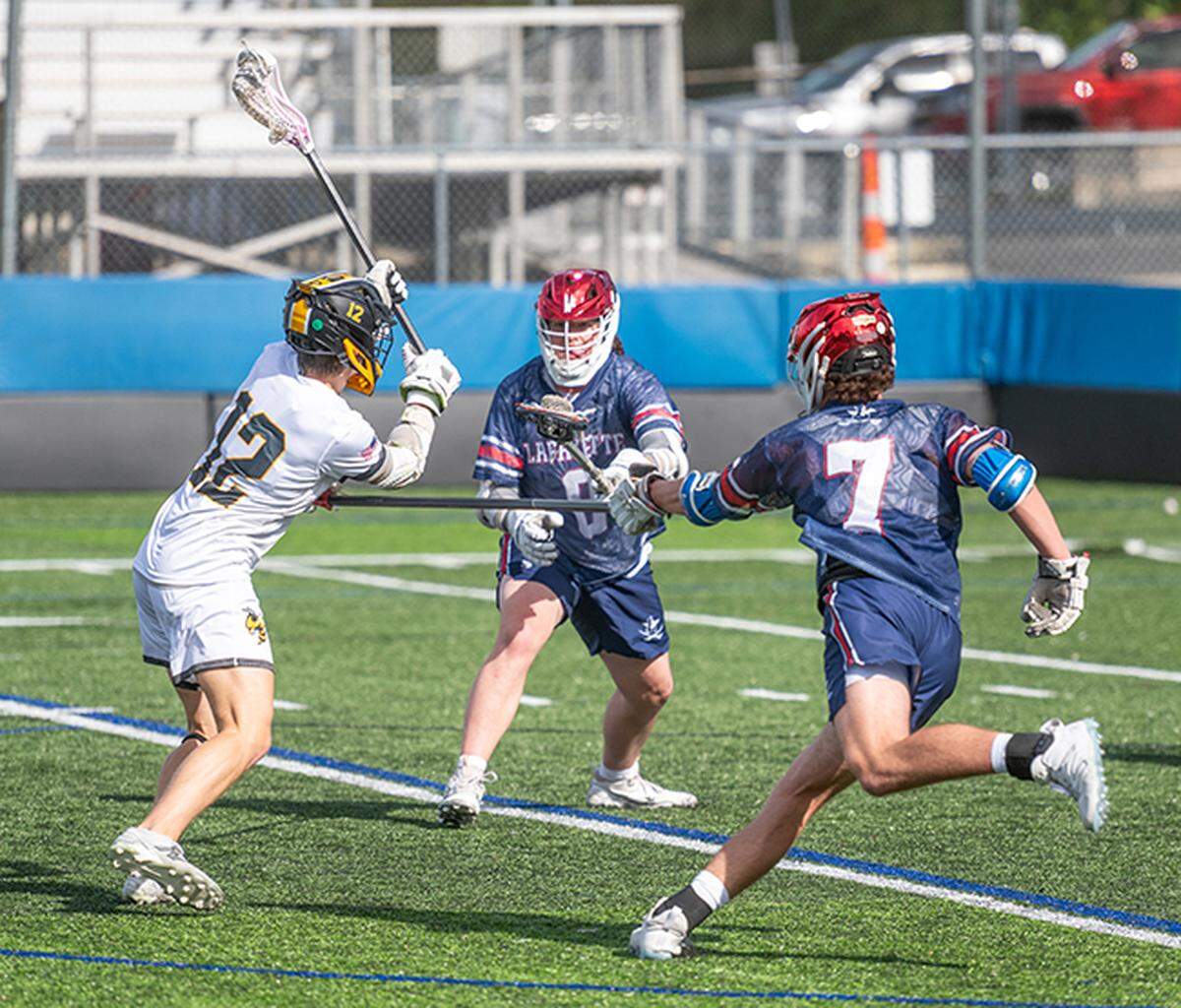 Woodford County’s Cole Humston (12) scores between Lafayette defenders Charlie Kerns (7) and Sam Morris (8) during the Yellow Jackets’ win in the 8th Region boys lacrosse semifinals at Lexington Catholic High School on Saturday.