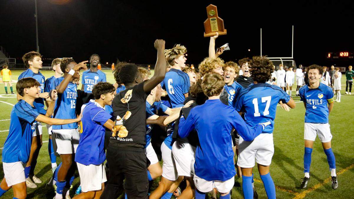 Henry Clay’s Marco Messerli brings the boys 42nd District Tournament championship trophy to his teammates after the Blue Devils’ 3-0 finals win against Frederick Douglass at The Farm on Friday.