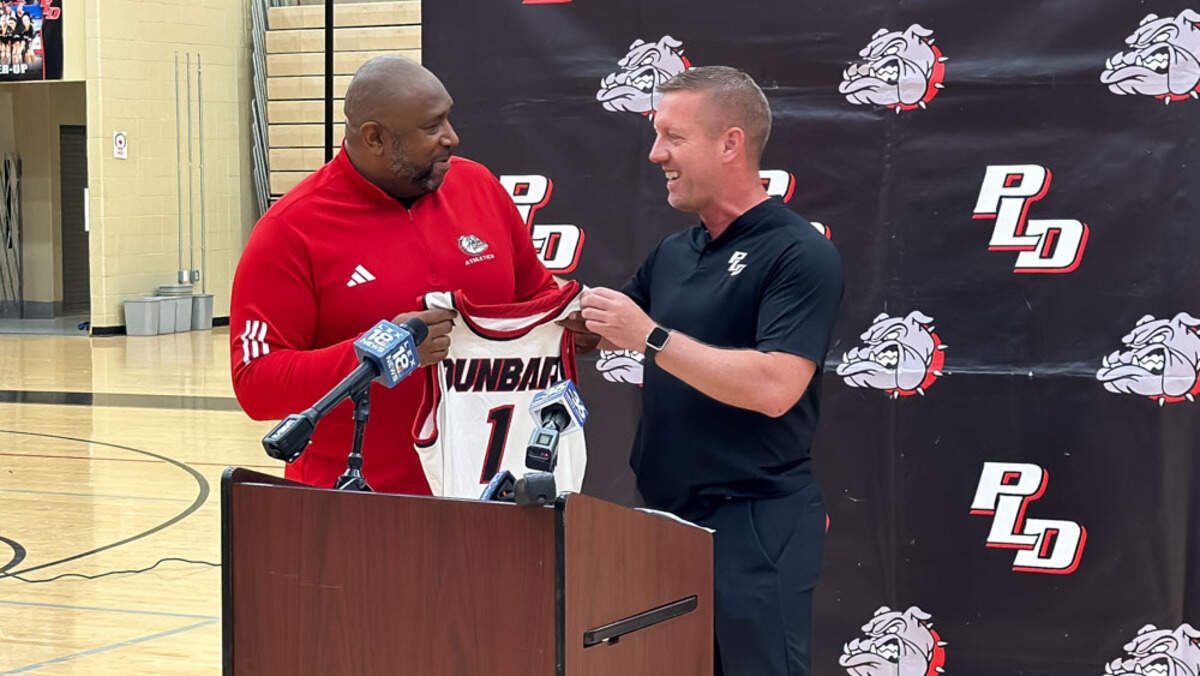 New Paul Laurence Dunbar High School boys basketball coach George Baker, left, accepts a Bulldogs jersey from athletic director Damon Kelley as Baker is introduced at a press conference at Dunbar’s S.T. Roach Sports Center on Wednesday.