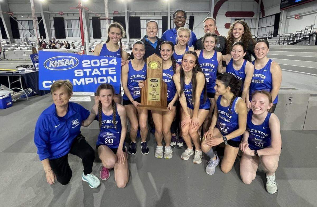 Lexington Catholic’s girls indoor track team, coached by Bernadette Madigan-Dugan, left, posed with their state championship trophy after winning the inaugural Class 2A KHSAA Indoor Track & Field State Championships at Norton Healthcare Sports & Learning Center in Louisville on Saturday.