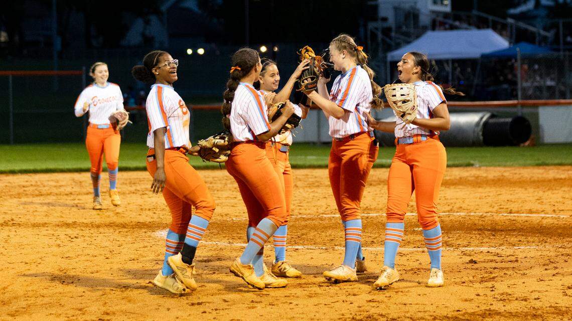 Frederick Douglass’ Emma Dunn and Haley McGuire, center left and right, touched gloves as their teammates gathered around to celebrate the Broncos’ 8-2 win over Scott County in the 42nd District Tournament softball championship game at Frederick Douglass High School on May 21, 2025.