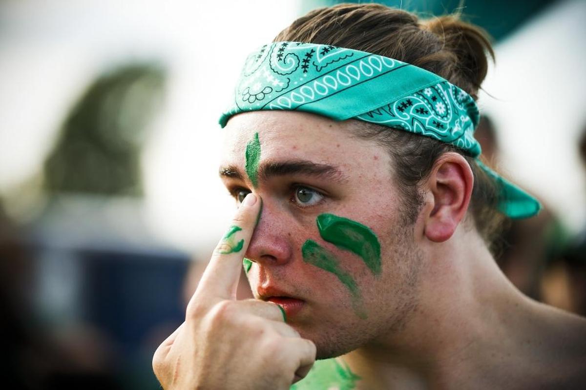 Chris Troutmam, of Louisville, Ky., a senior at Trinity, applies paint to his face while tailgating with other students before a game between Trinity and St. Xavier at Papa John's Cardinal Stadium in Louisville, Ky., Friday, Sept. 29, 2017. Trinity beat St. Xavier 28-0.