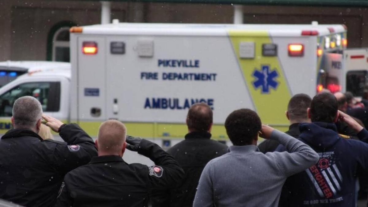 Police officers salute as Scotty Hamilton’s flag-draped casket is taken to a funeral home in downtown Pikeville.