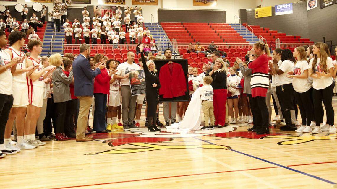 Scott County High School unveiled a plaque and framed red blazer at the dedication of the new Coach Billy Hicks Gymnasium at the school in Georgetown on Wednesday. Betsy Hicks, center, the wife of the late coaching legend, acknowledged those gathered for the dedication current and former players gathered as center court. Former players Scott Hundley, left of Mrs. Hicks, and Michael Moreno, held the plaque and framed blazer respectively. Hicks’ grandson, Wyler Nash Johnson, helped pull away the cloth draping the frame as his mother, Ashley Johnson (black top) looked on.