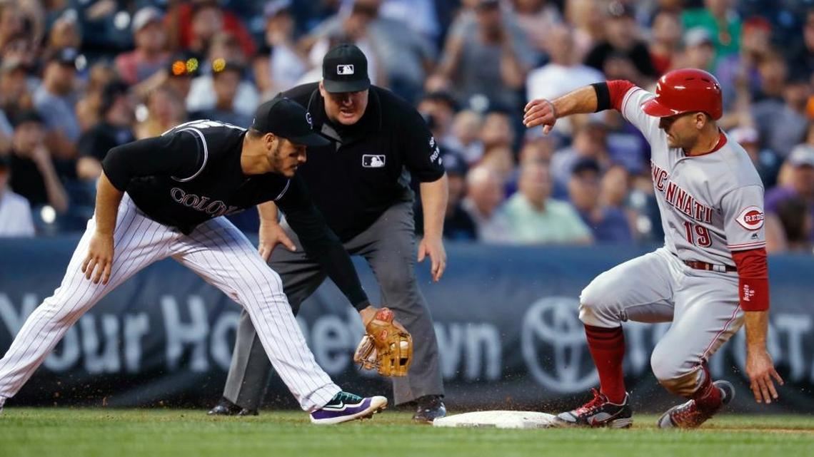 Colorado Rockies third baseman Nolan Arenado, left, turns to apply a late tag as the Cincinnati Reds’ Joey Votto advances to third base on a Scooter Gennett single as third base umpire Bill Miller watches during the sixth inning of the Rockies’ 5-3 win Wednesday, July 5, 2017, in Denver.