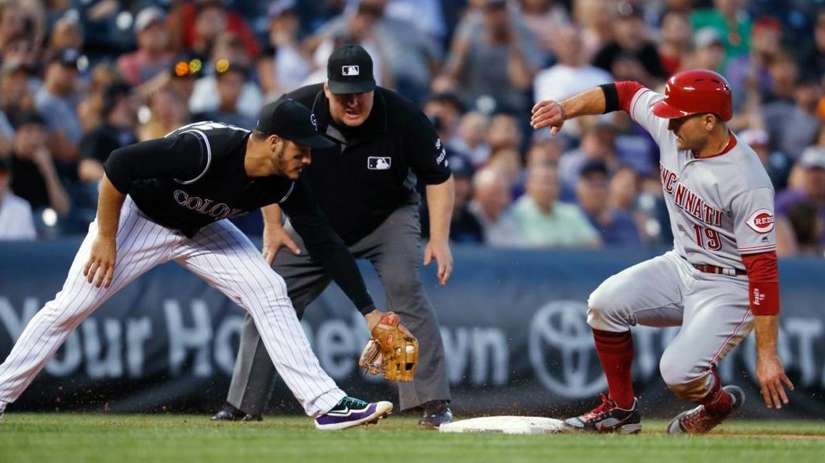 Colorado Rockies third baseman Nolan Arenado, left, turns to apply a late tag as the Cincinnati Reds’ Joey Votto advances to third base on a Scooter Gennett single as third base umpire Bill Miller watches during the sixth inning of the Rockies’ 5-3 win Wednesday, July 5, 2017, in Denver.